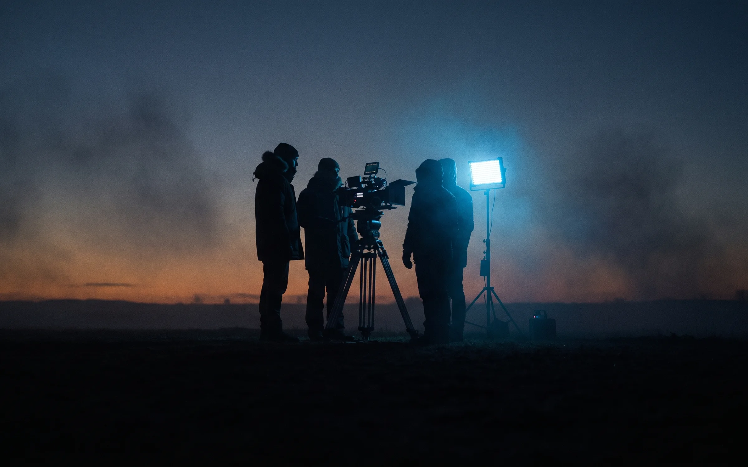 A small crew around the camera at dusk on the set of The Weave
